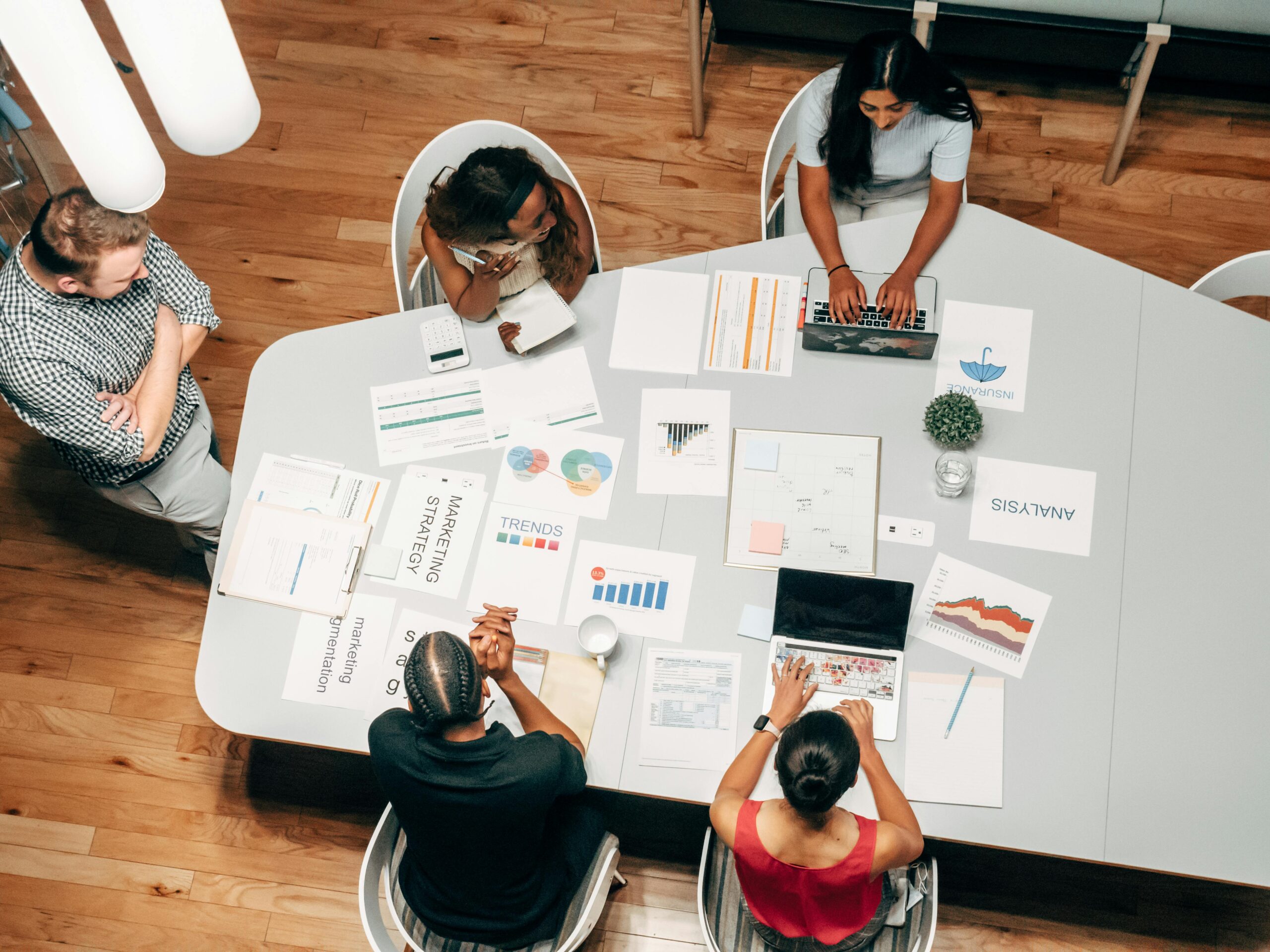 Marketing team collaborating around a conference table reviewing strategy documents, analytics reports, and performance charts